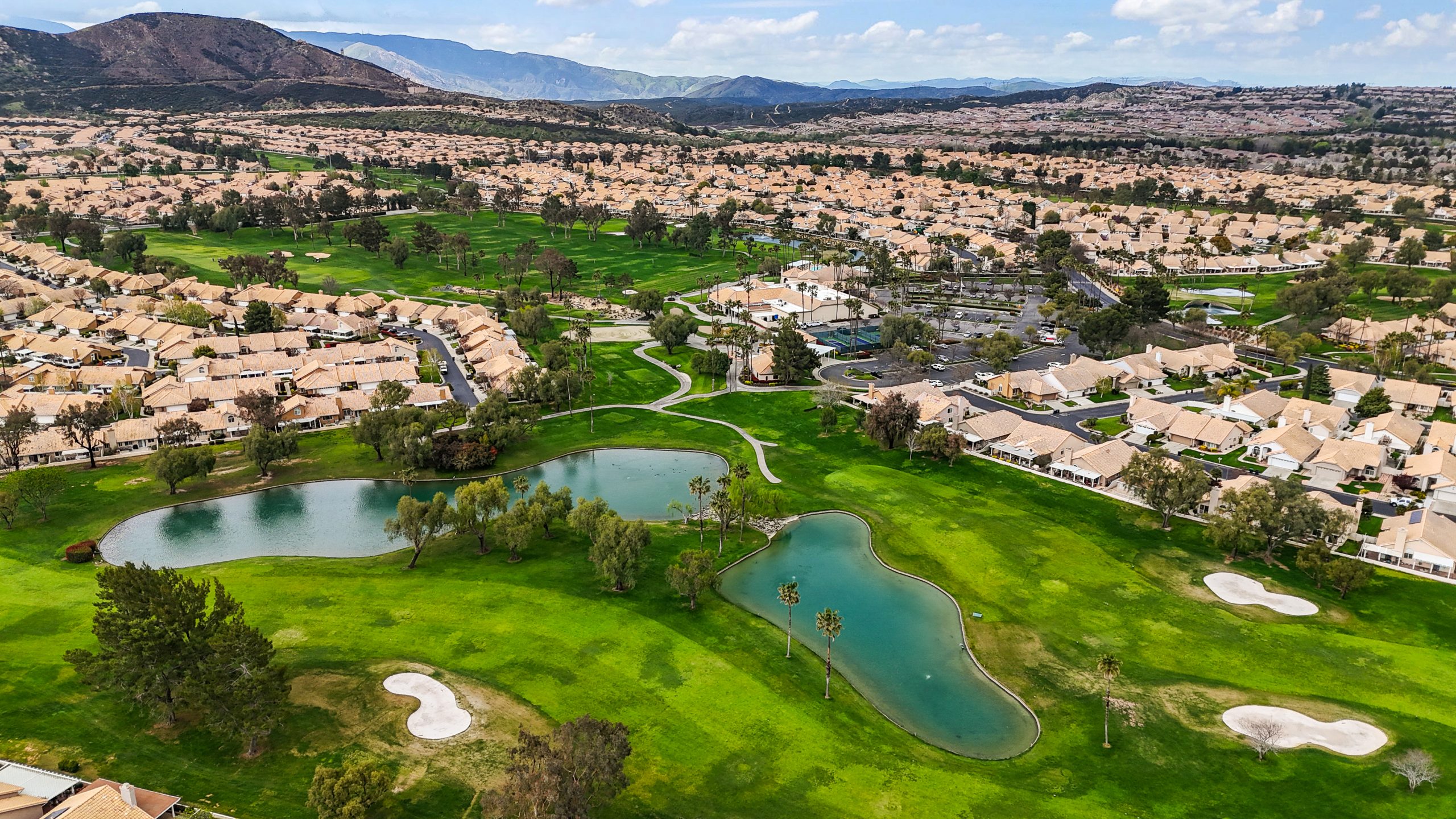 Aerial view of Sun Lakes Country Club in Banning, CA, showing residential homes alongside green fairways, water features, and mountain views.